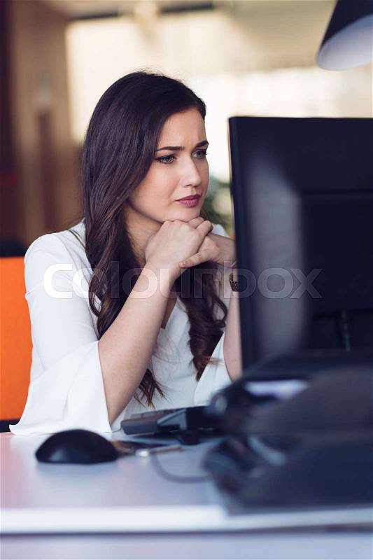 Concentrated middle aged woman working on her computer. Start-up office background, stock photo