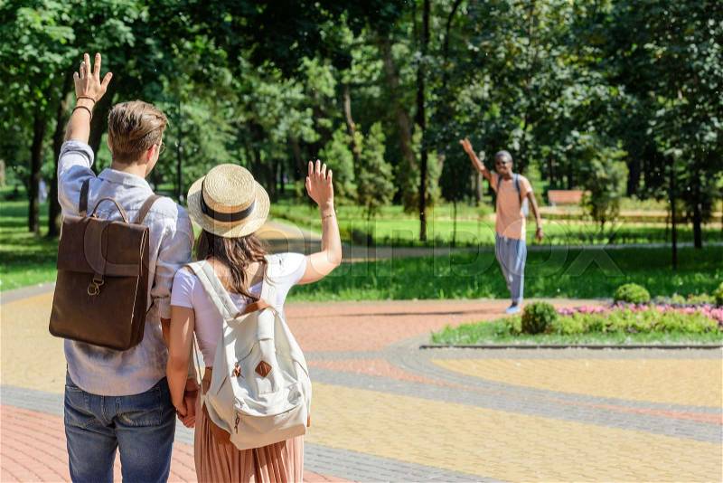Back view of couple waving to african american man in park, stock photo