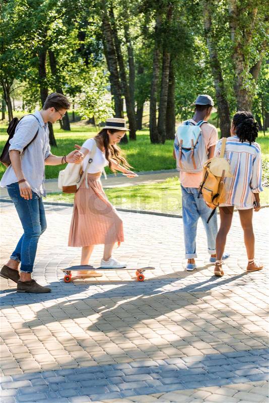 Man helping young woman ride longboard while african american couple walking in front, stock photo