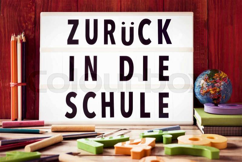 The text zuruck in die schule, back to school in german, in a lightbox placed against a rustic wooden background, surrounded by three-dimensional numbers and chalks and pencils of different colors, stock photo