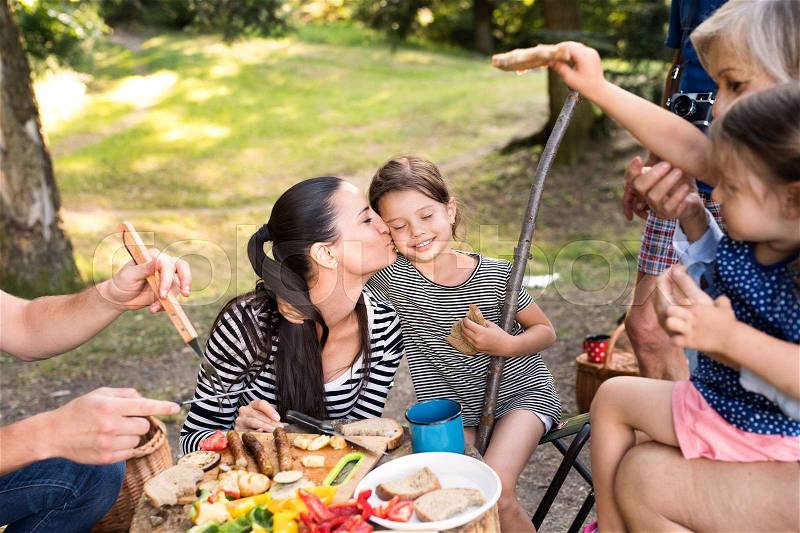 Beautiful family enjoying camping holiday in forest, eating together. Barbecue with drinks and food, stock photo