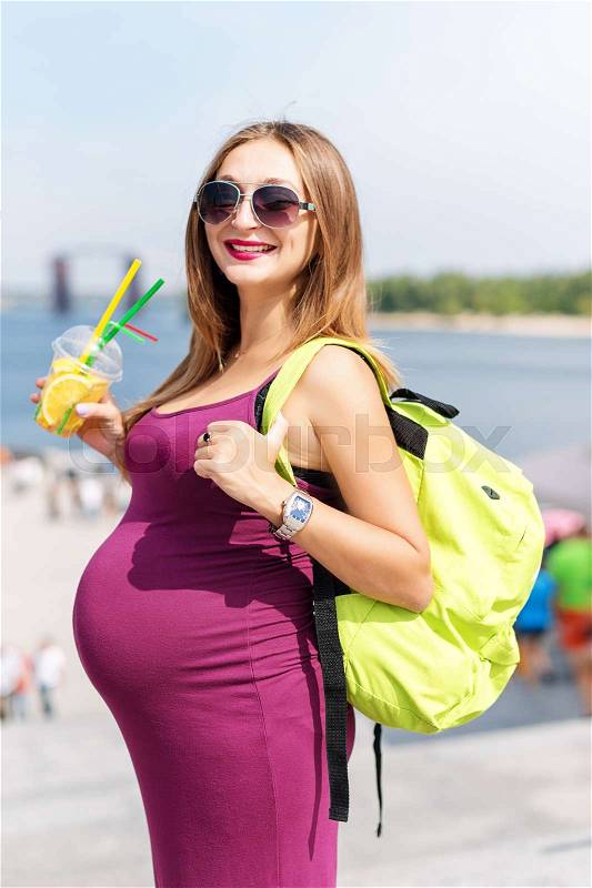Pretty young pregnant woman drinking juice and enjoying her walking on the city embankment. Woman tourist, active and healthy pregnancy and lifestyle, tourism and travelling abroad, stock photo
