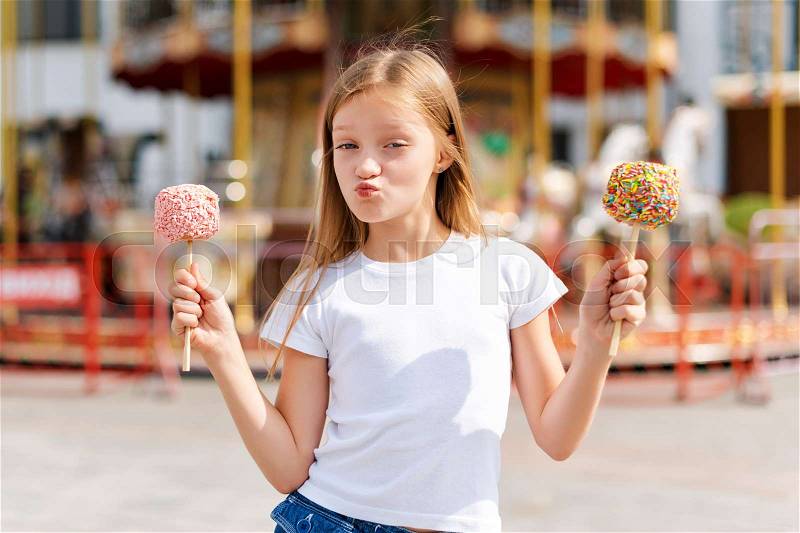 Cute little girl eating candy apple at fair in amusement park, stock photo