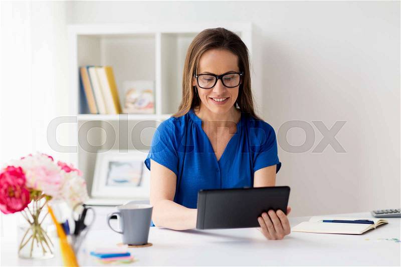 Business, people and technology concept - happy smiling woman in glasses with tablet pc computer working at home or office, stock photo