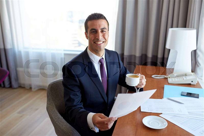 Business trip, people and paperwork concept - happy smiling businessman with papers drinking coffee at hotel room, stock photo