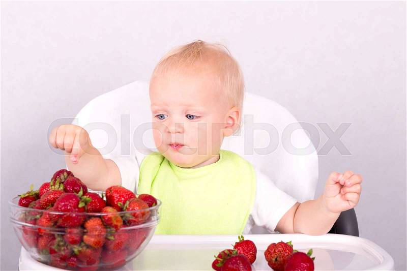 Blue eyed funny toddler choosing strawberries. Cute baby boy eating strawberries, stock photo