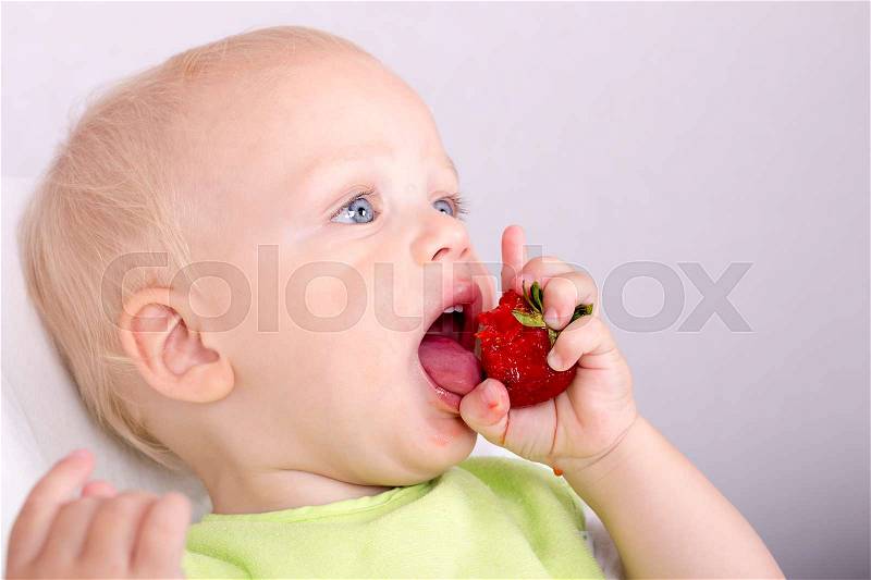 Cute toddler eating a ripe strawberry. Funny baby boy Tasting ripe berries, stock photo