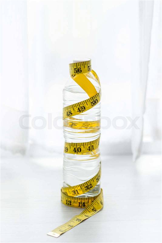 A bottle of water with measuring tape on the floor near window. Health concept, stock photo