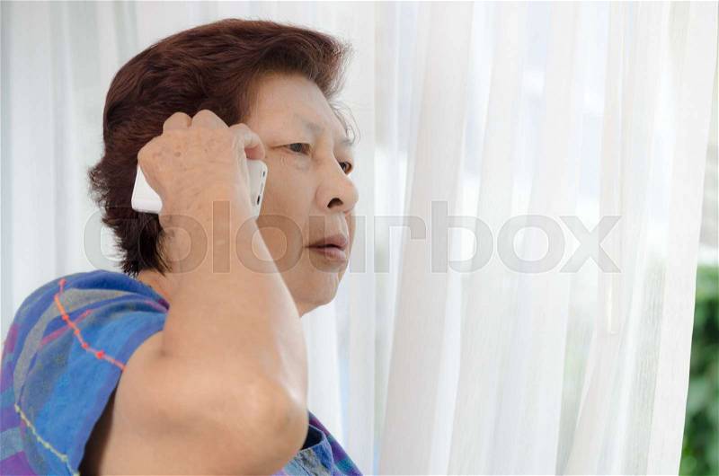 Asian senior woman using a phone call near window at home, stock photo