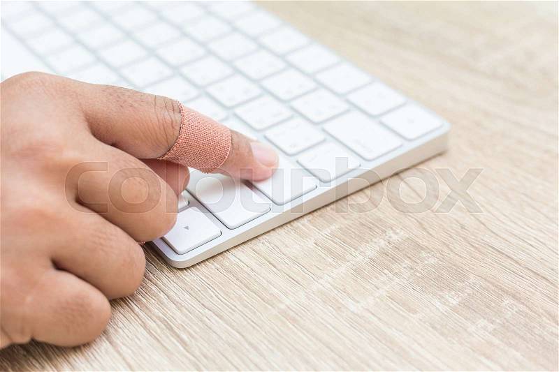 Close up hand with injury on finger using white computer keyboard on wooden background, stock photo
