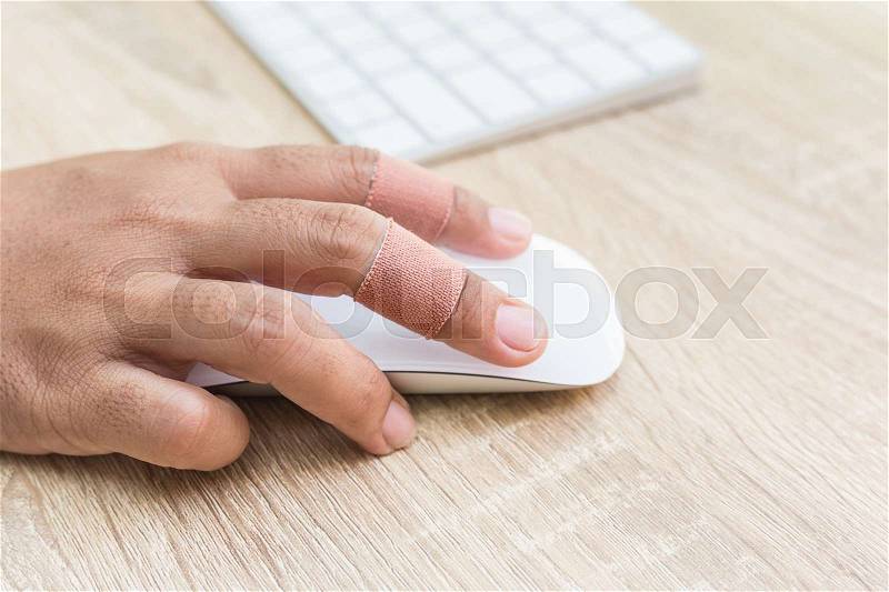 Close up hand with injury on finger using white computer wireless mouse on wooden background, stock photo