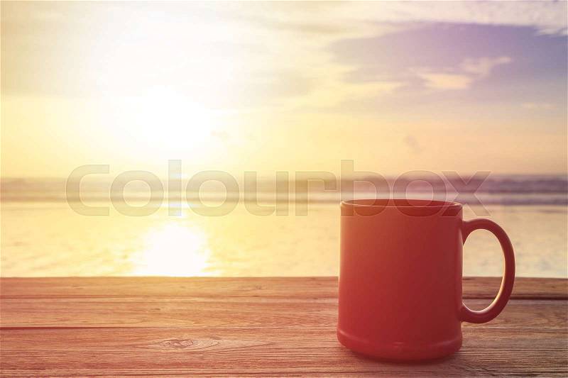 Close up red coffee cup on wood table at sunset or sunrise beach, stock photo