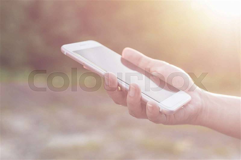 Close up hand of woman holding or using smartphone on green blur and sunlight effect, stock photo