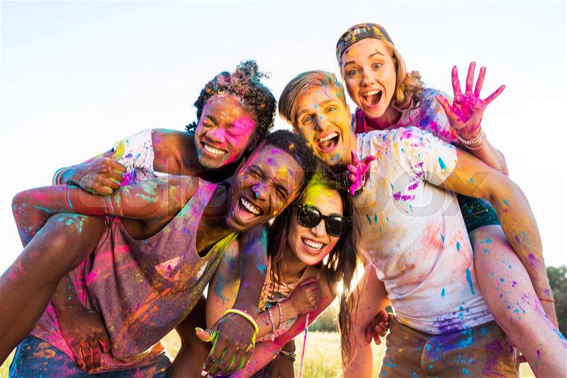 Happy young multiethnic friends with colorful paint on clothes having fun together at holi festival , stock photo