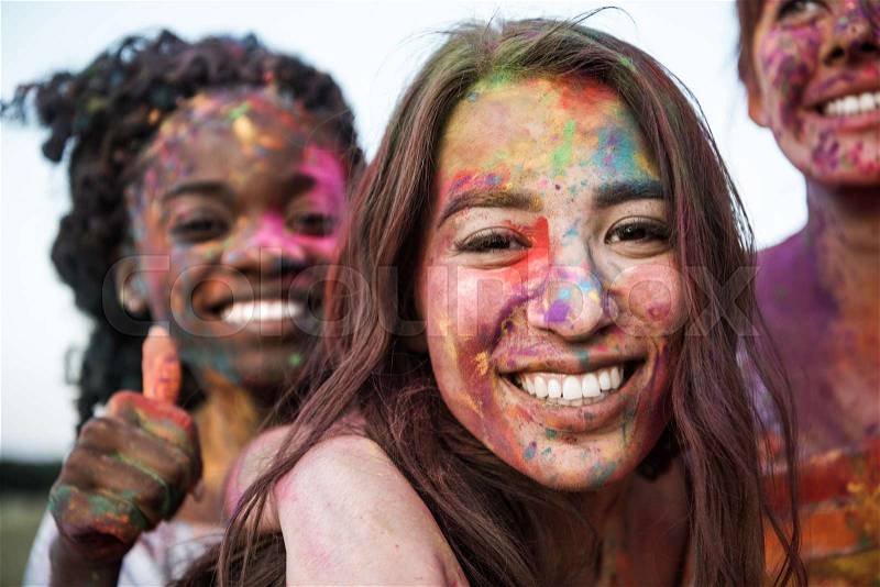 Happy young multiethnic women with colorful paint on clothes and bodies having fun together at holi festival, stock photo