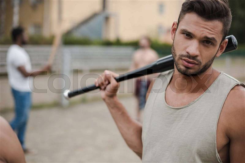 Young handsome man posing with baseball bat on court, stock photo