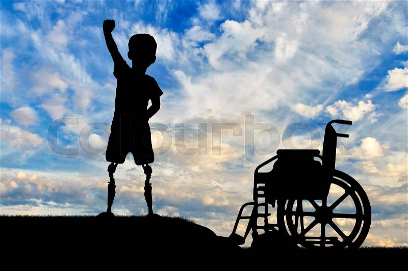Children with disabilities concept. Happy disabled boy with a prosthetic legs standing near a wheelchair against the sky, stock photo