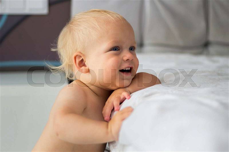 Cute blue eyed smiling baby boyin his room. Funny smiling toddler against the bed, stock photo