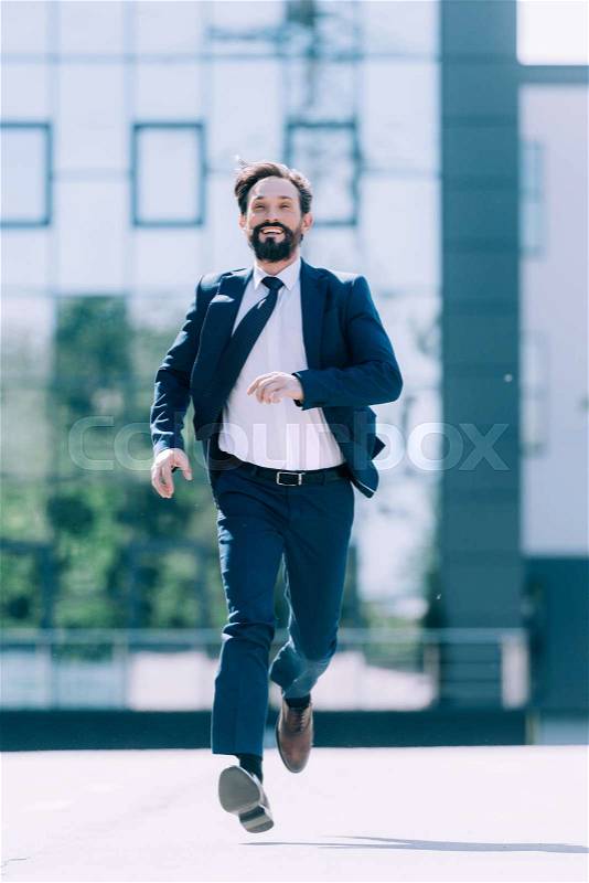 Handsome bearded mature businessman in suit running on the street, stock photo