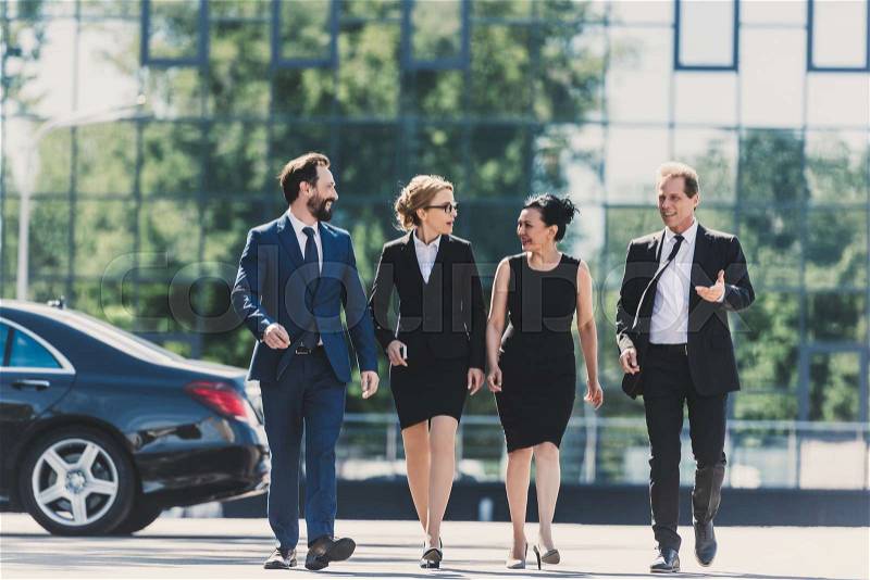 Professional team of middle aged multiethnic businesspeople walking together and talking in city, stock photo
