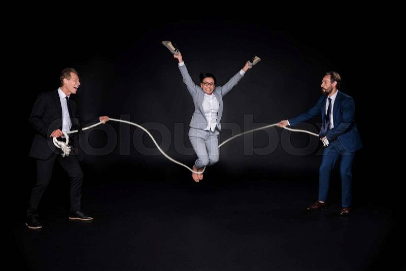Businessmen holding rope while mature barefoot asian businesswoman jumping isolated on black, stock photo