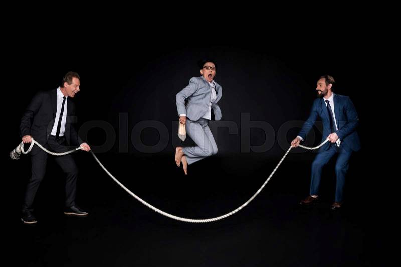 Businessmen holding rope while mature barefoot asian businesswoman jumping isolated on black, stock photo