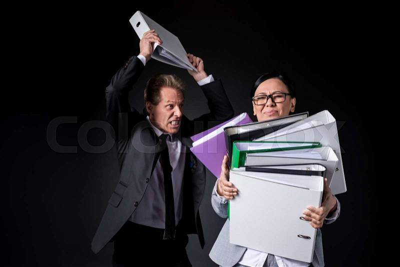 Overworked mature businesswoman holding folders while angry male colleague able to hit isolated on black, stock photo