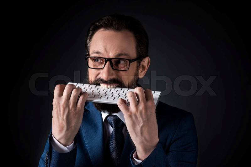 Nervous bearded mature businessman biting keyboard isolated on black, stock photo