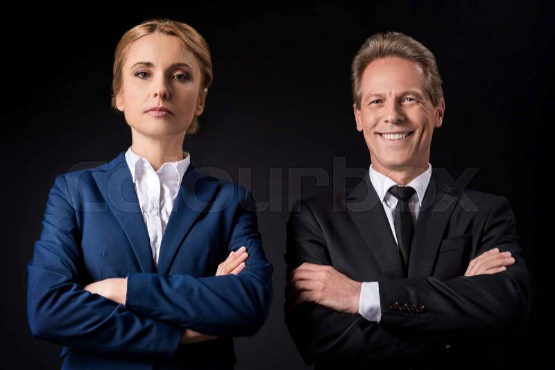 Confident mature business people standing with crossed arms and looking at camera isolated on black , stock photo