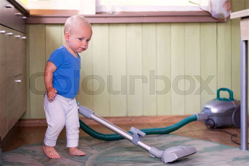 Funny toddler cleaning up the kitchen with hoover, stock photo