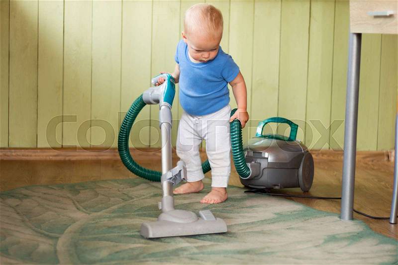 Cute toddler cleaning up the kitchen with hoover, stock photo