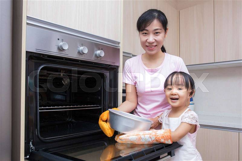 Asian Chinese mother and daughter baking cake together at home in the kitchen, stock photo