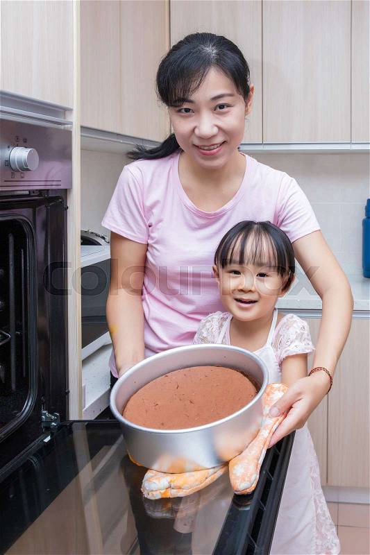 Asian Chinese mother and daughter baking cake together at home in the kitchen, stock photo