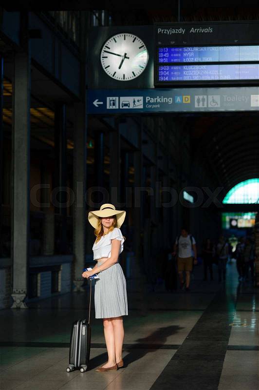 Charming girl in sun-hat in the waiting room of the train station. Nearby is a suitcase. In hand her passport and tickets. Time of summer holidays, stock photo