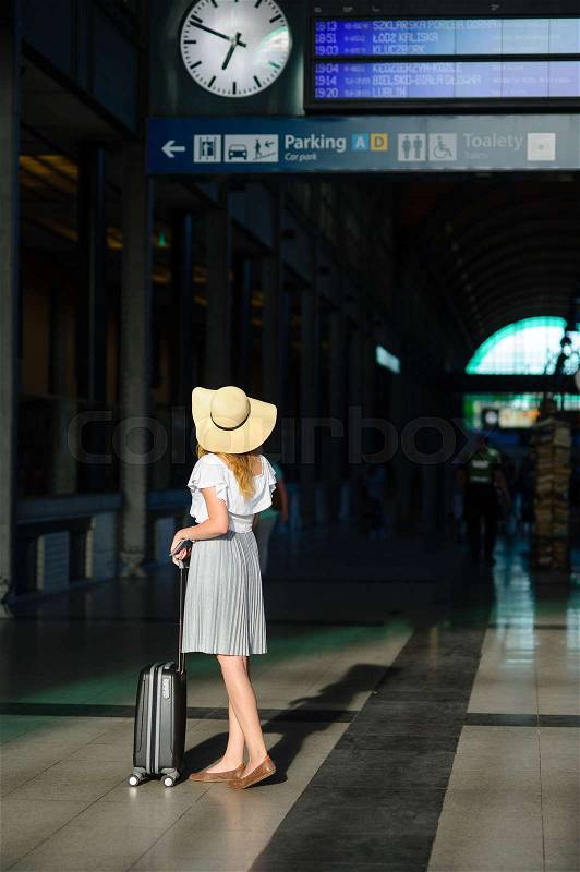 Girl in a sun-hat in the waiting room of the railway station. The tourist is study the train schedule. Time of summer holidays, stock photo