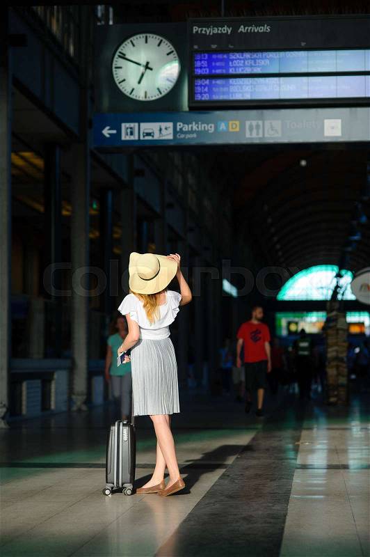 Girl in a sun-hat in the waiting room of the railway station. The tourist is study the train schedule. Time of summer holidays, stock photo