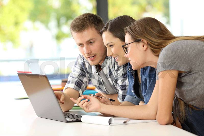 Three students learning together on line with a laptop in a classroom, stock photo