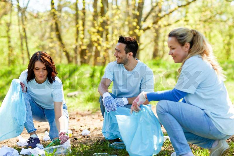 Volunteering, charity, people and ecology concept - group of happy volunteers with garbage bags cleaning area in park, stock photo