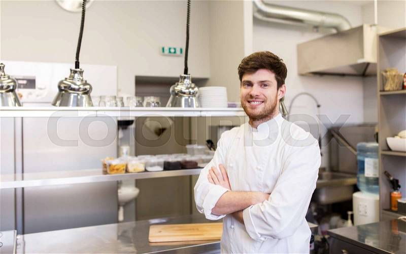 Cooking, profession and people concept - happy male chef cook with crossed hands at restaurant kitchen, stock photo