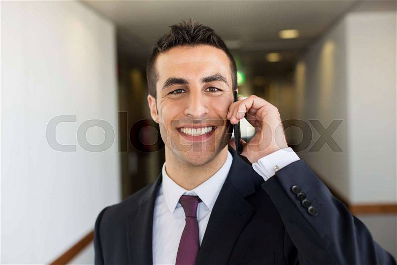 Business trip, people and communication concept - happy smiling businessman calling on smartphone at hotel corridor, stock photo