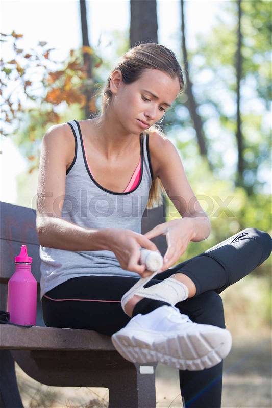 Woman applying compression bandage on her leg after injury, stock photo