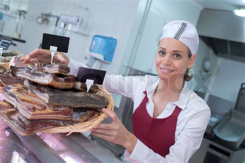 Female butcher with ham in meat store counter, stock photo