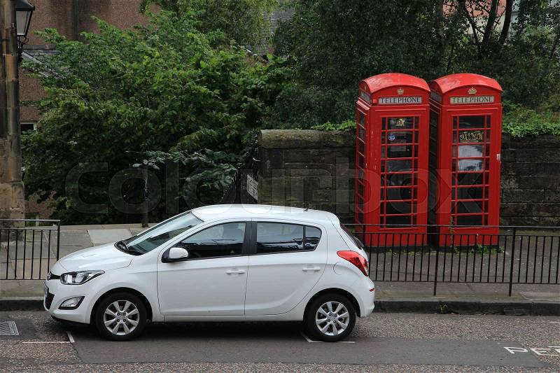 Two famous red telephone booths and a white car in one of the streets in the city Edinburgh in Scotland in the summer, stock photo