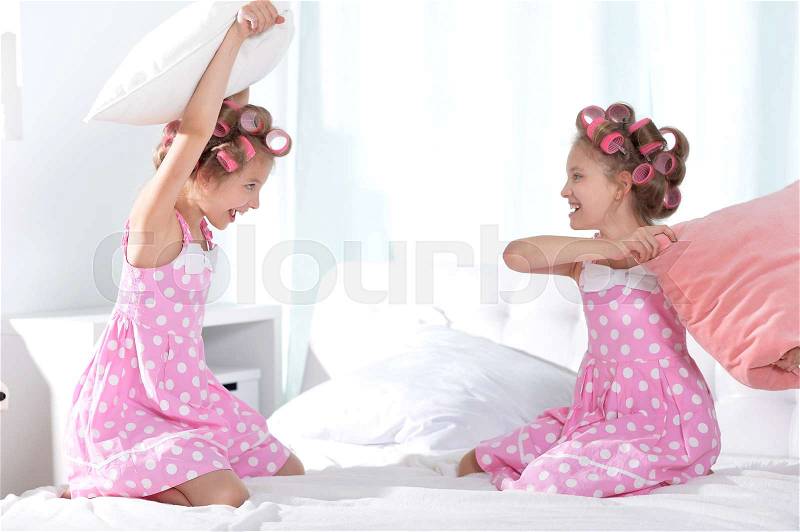 Cute tweenie girls in hair curlers playing with pillows with at home, stock photo