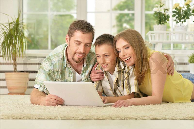 Happy family lying on carpet and using laptop together at home, stock photo