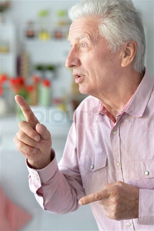 Happy elderly man pointing up at home, stock photo
