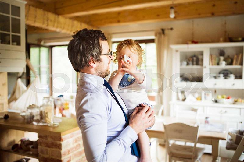 Young businessman coming home from work, in the kitchen with his little son holding him in the arms, stock photo