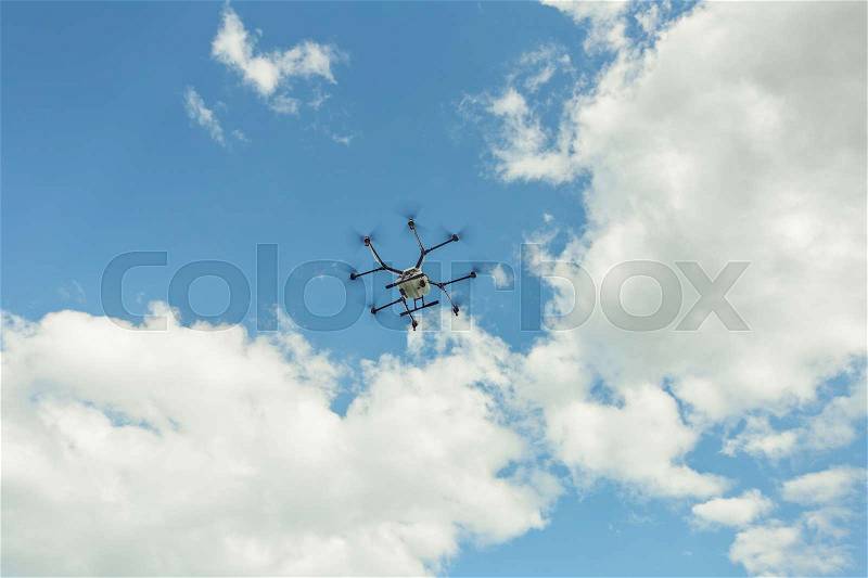 Hovering drone flies in blue sky and taking pictures of green hills. Professional agriculture drone flying in clear blue. Sky partly clouded, stock photo