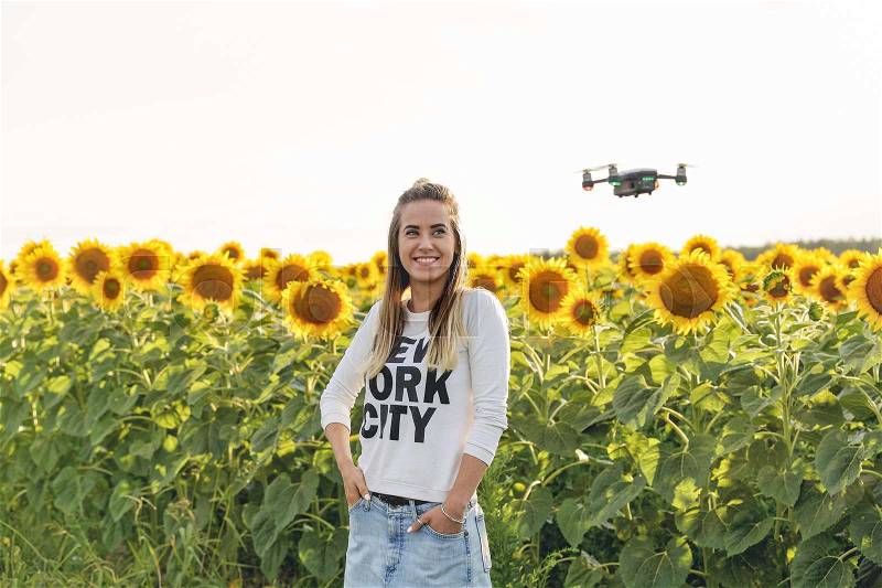 Beautiful young woman doing selfie on a mini drone in the background of a beautiful landscape. The girl stands against the background of a field of sunflowers, stock photo