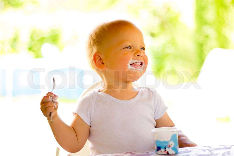 Happy one year kid eating a yogurt or sour cream against blurred nature background, stock photo